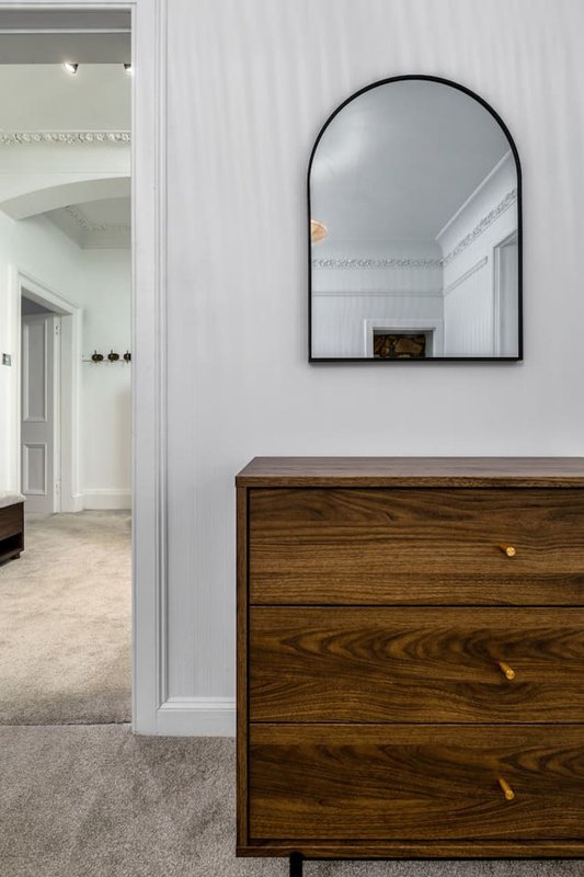 Modern hallway with wooden dresser, arched mirror and white walls