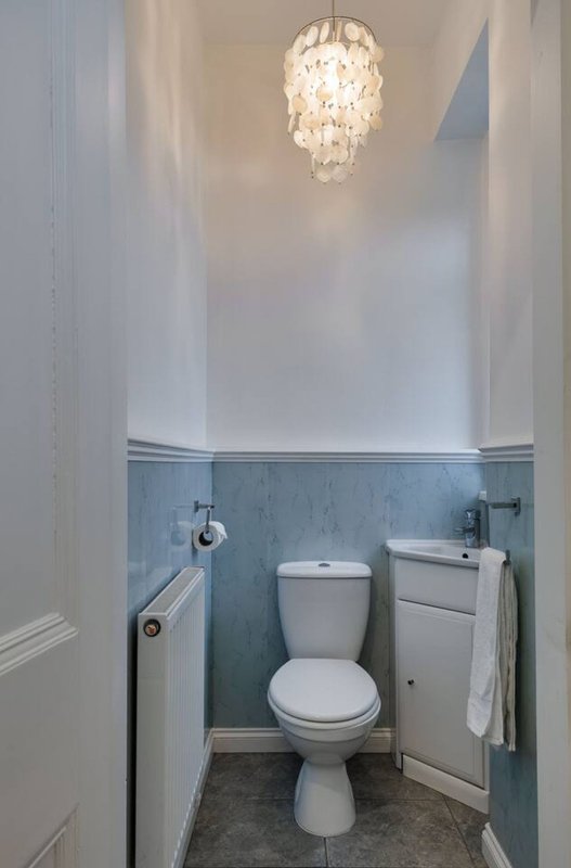Small bathroom with toilet, sink, blue-grey wall panelling and crystal pendant light