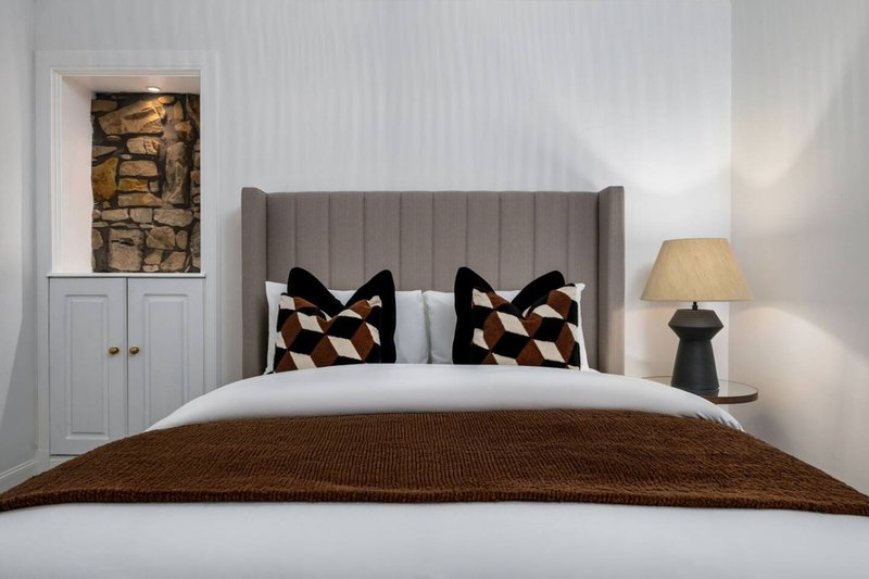 Modern bedroom with upholstered headboard, neatly made bed, patterned cushions, and contemporary lamp