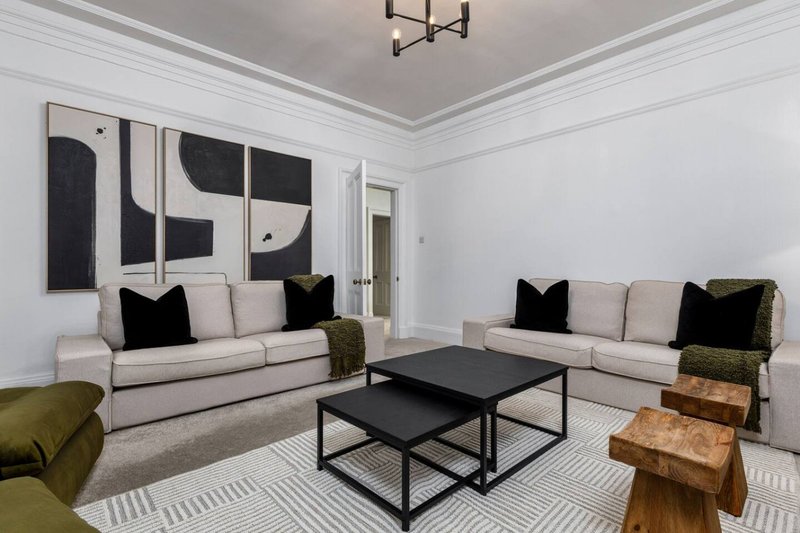Spacious living room with two cream sofas, black coffee table, modern artwork and olive armchair