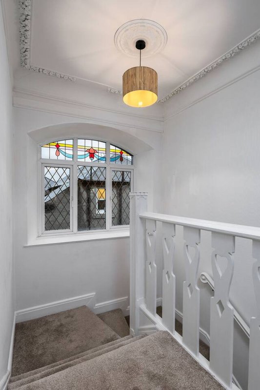 Bright hallway with white walls, wooden pendant light, decorative window and white railing