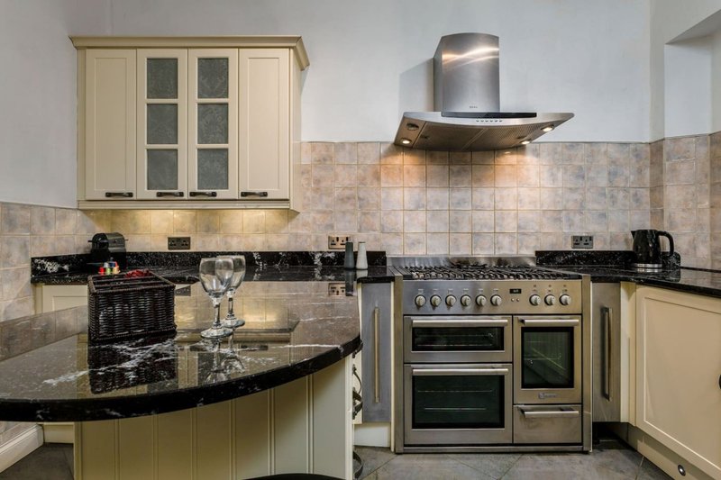 Cream and black kitchen with curved island, dual oven range, and tile backsplash