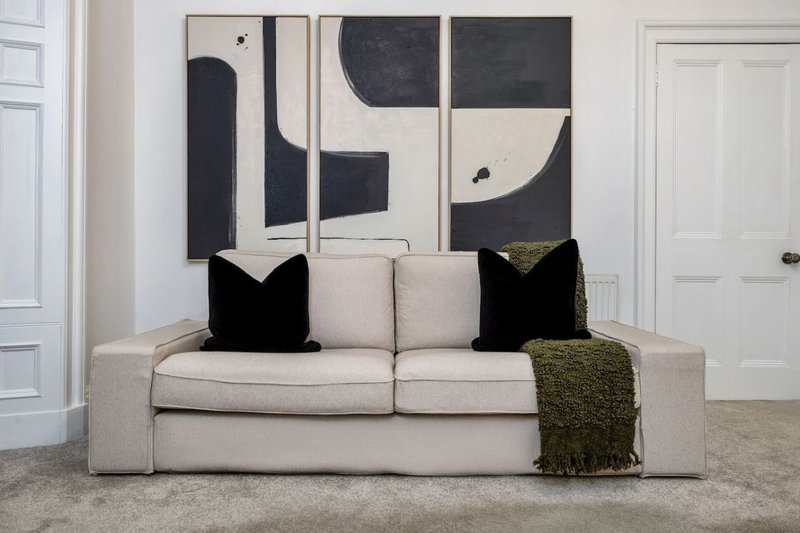 Modern living room with beige sofa, black cushions, olive throw, and abstract wall art