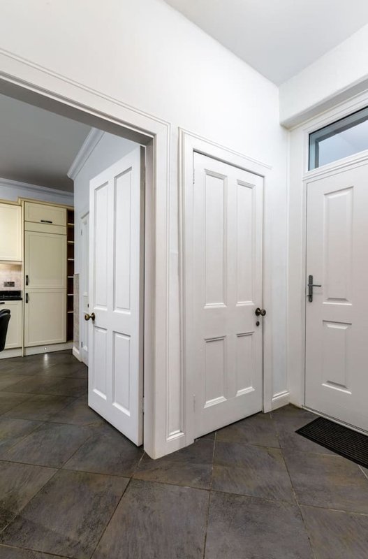 Hallway with white panel doors, dark tile flooring, and kitchen visible in background
