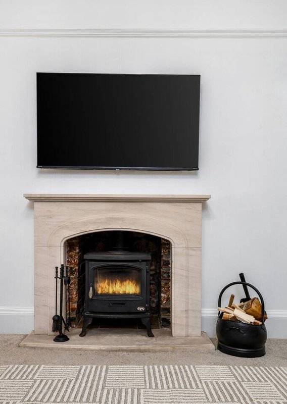 Fireplace with black stove insert, cream surround, wall-mounted TV above, and black kettle beside
