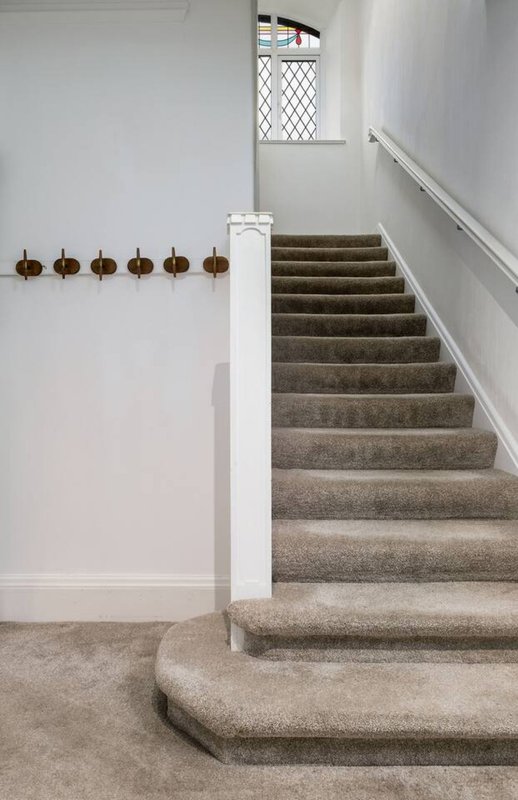 Staircase with carpet treads, white walls, brass coat hooks, and diamond-patterned window