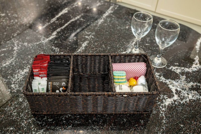 Woven basket with organised items including napkins, glasses and decorative accessories on speckled countertop