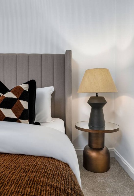 Modern bedroom with upholstered headboard, double bed, decorative cushion, and bedside lamp
