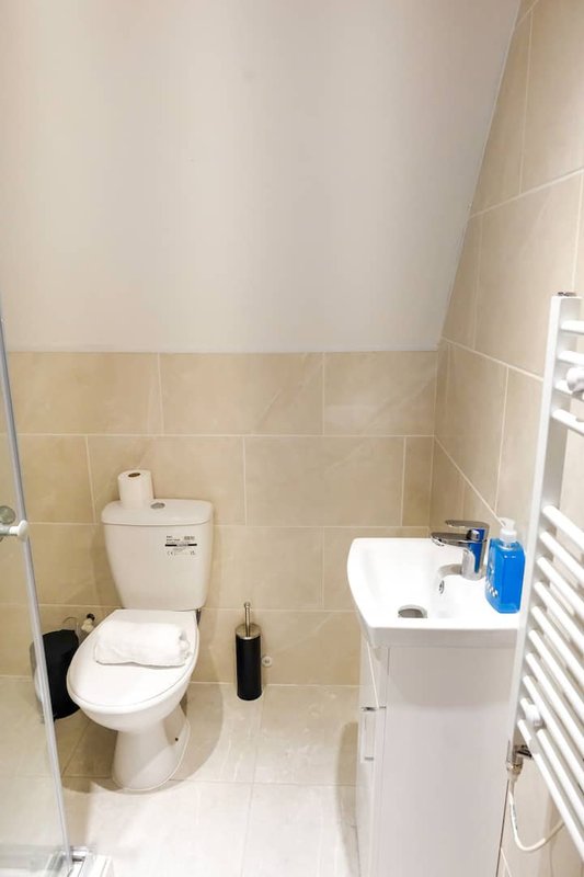 Small bathroom with toilet, pedestal sink, heated towel rail and beige tile walls