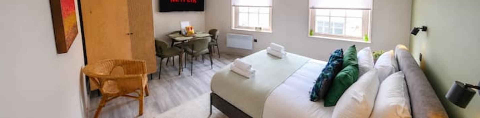 Bright bedroom with double bed, wicker chair, dining table, and large windows