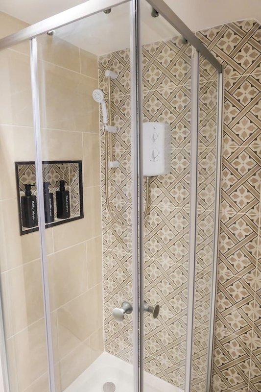 Modern bathroom shower with glass enclosure, patterned tile walls and built-in shelving