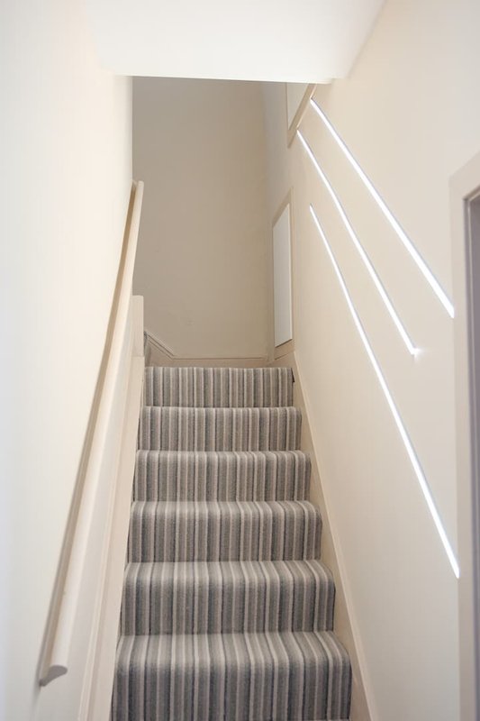 Staircase with striped carpet runner, white walls, handrail and natural light from window