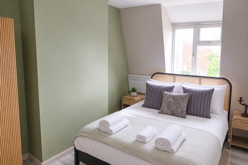Bright bedroom with double bed, striped pillows, white bedding and green accent wall