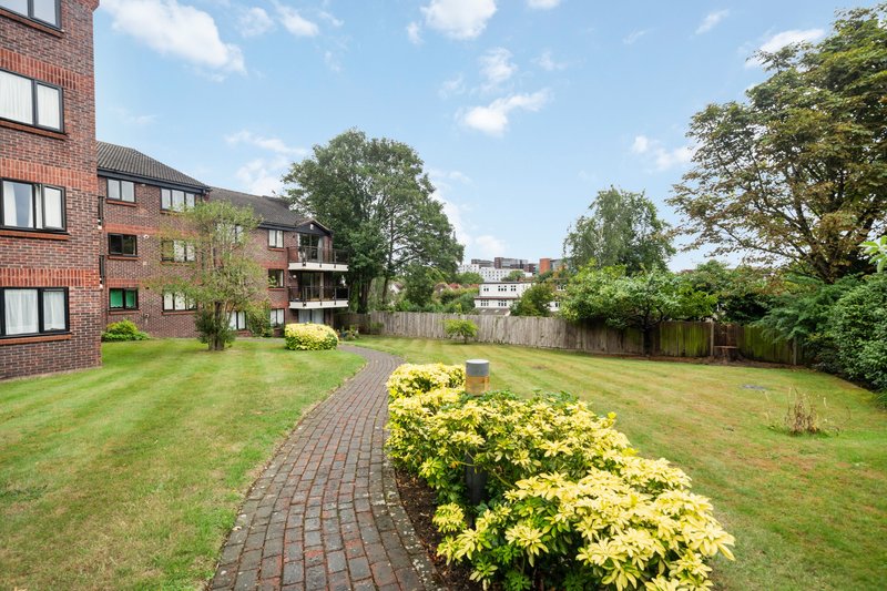 Communal garden with brick pathway, manicured lawn, yellow flowering shrubs and red brick apartment building