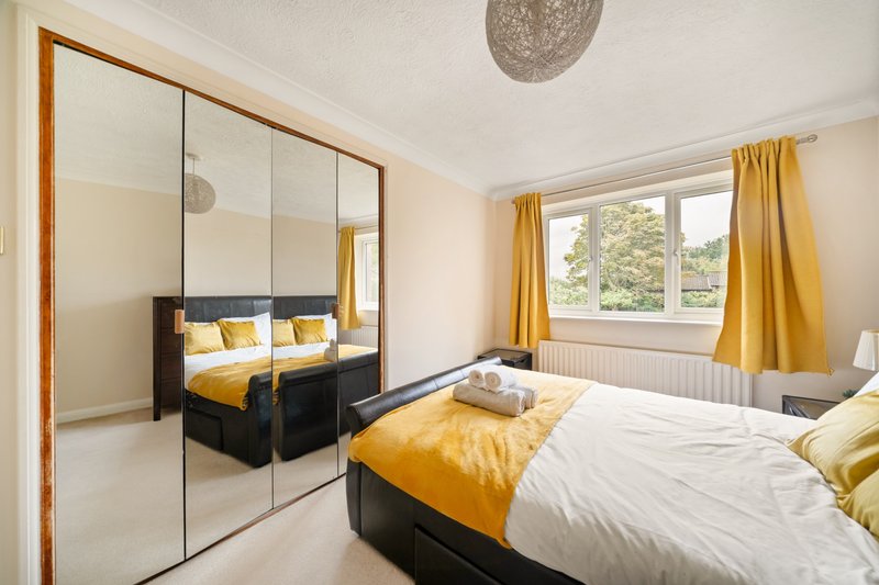 Bright bedroom with double bed, mirrored wardrobe, yellow bedding and curtains, window with garden view