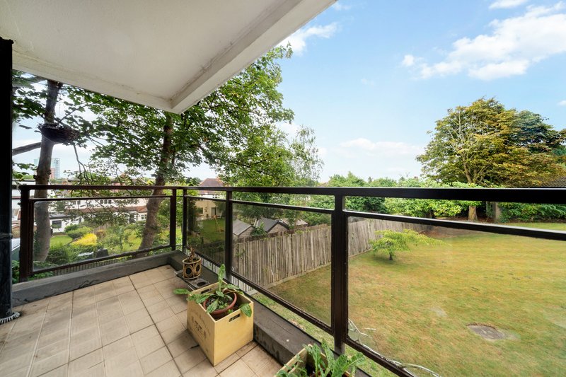 Covered balcony with black railing overlooking garden and trees with potted plants