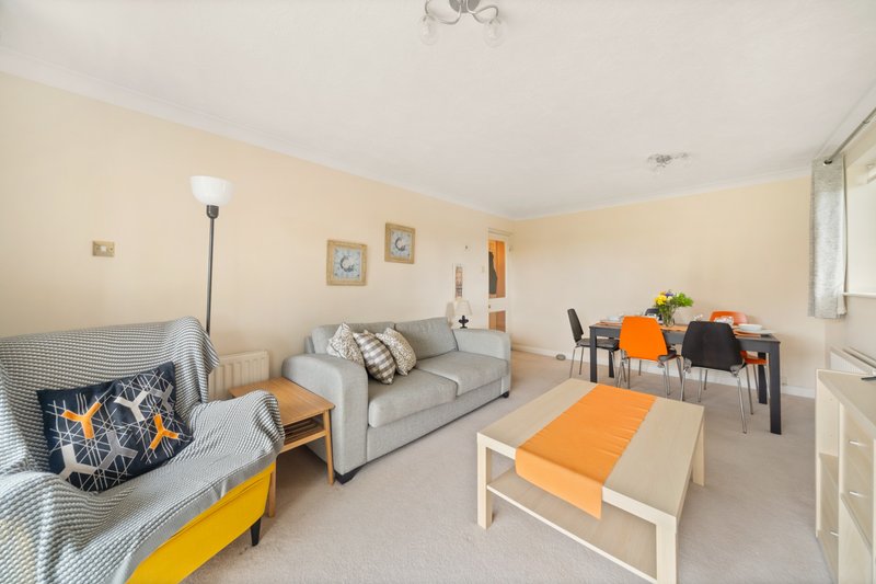 Bright living room with sofa, armchair, coffee table and dining area with orange accents