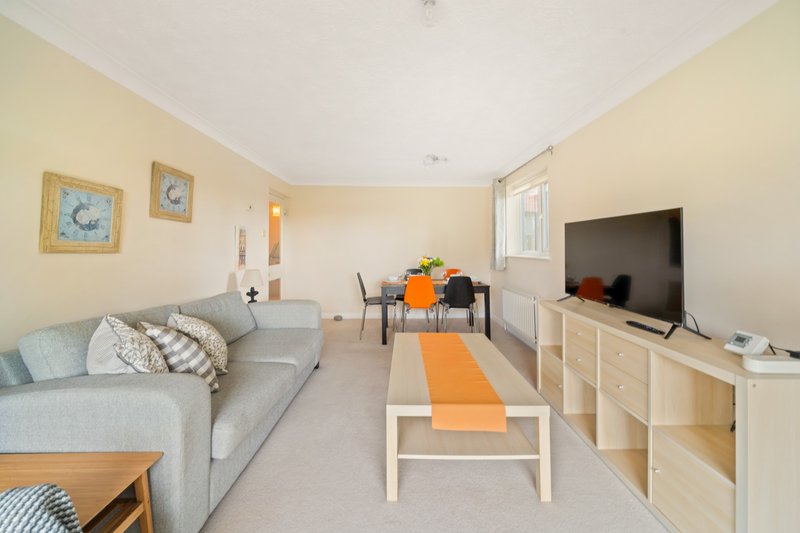 Bright open-plan living room with gray sofa, TV unit, dining area and orange accents