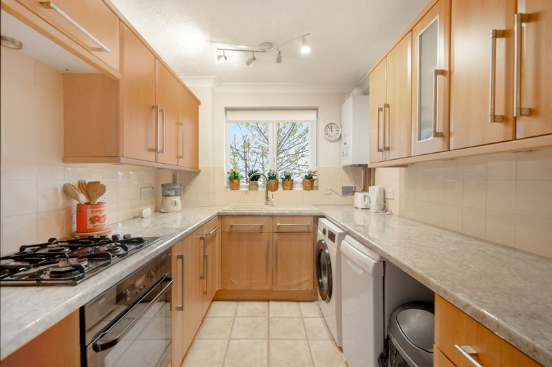 Modern kitchen with wooden cabinets, gas hob, washing machine, dishwasher and window with potted plants