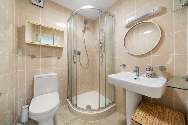 Modern ensuite bathroom with corner shower, toilet, sink and round mirror