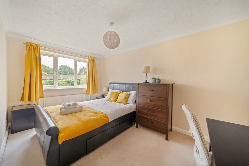 Bright bedroom with double bed, wooden chest of drawers, yellow curtains and pendant light