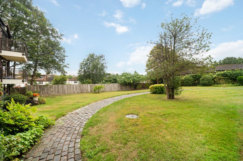 Large garden with paved pathway, mature trees, and house visible on left side