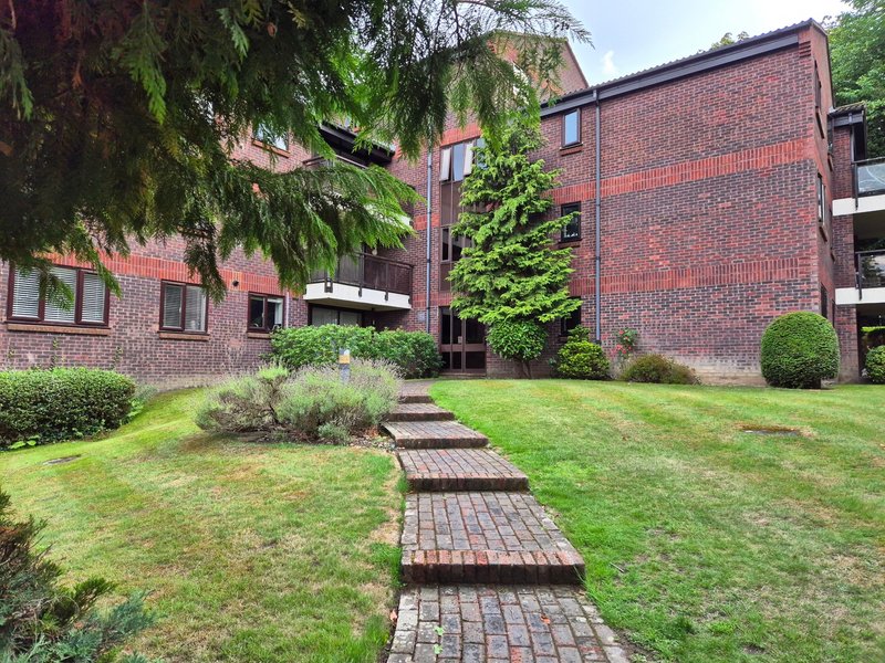 Brick apartment building with manicured garden, lawn, and brick pathway leading to entrance