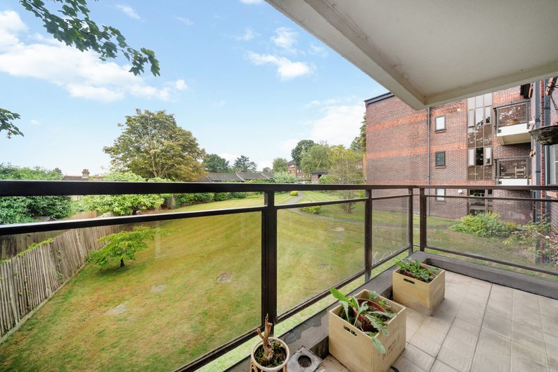 Balcony with black railing overlooking green garden and brick residential building