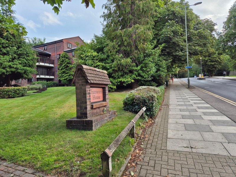 Brick apartment building with manicured lawn, wooden fence, and street view