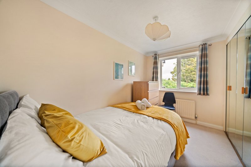 Bright bedroom with double bed, yellow bedding, built-in wardrobes and window with garden view