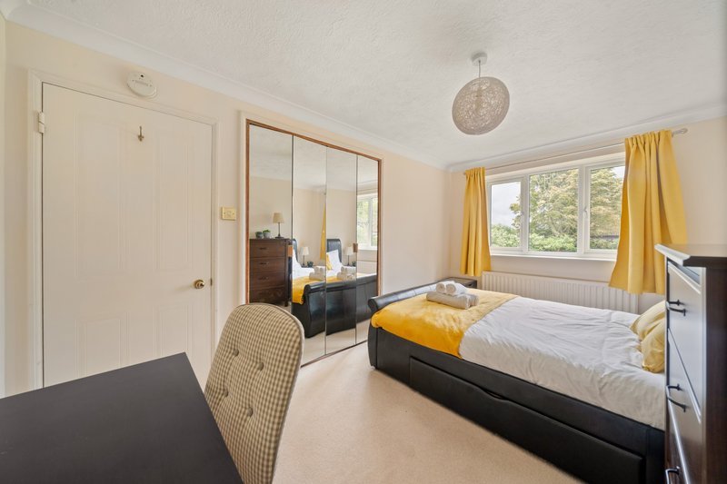 Bright bedroom with double bed, yellow curtains, mirrored wardrobe and work desk