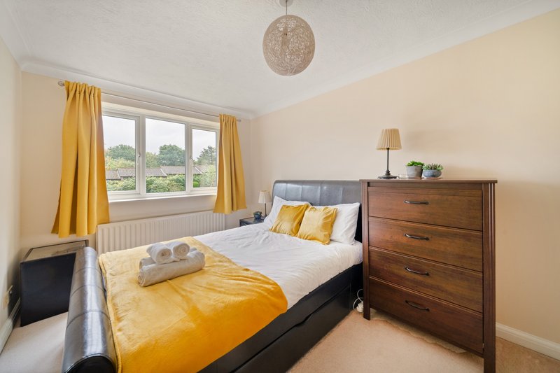 Bright bedroom with double bed, yellow bedding, wooden dresser and garden views