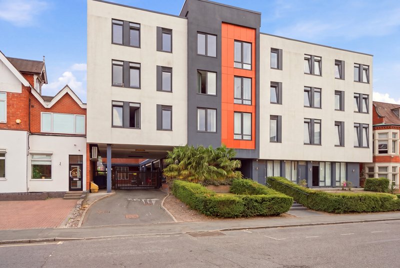 Modern apartment building with cream and orange facade, ground-floor retail space, curved driveway and landscaping
