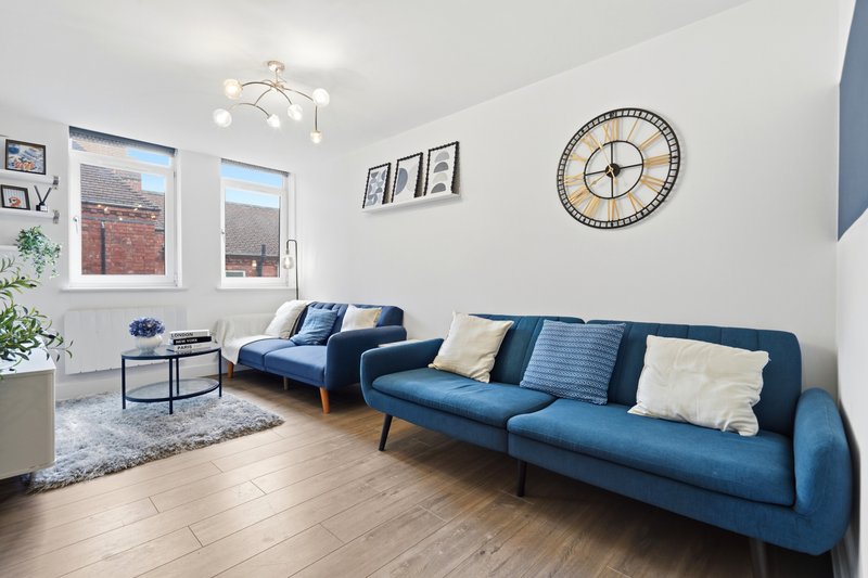 Bright living room with blue sofa, armchair, wooden floor and large windows