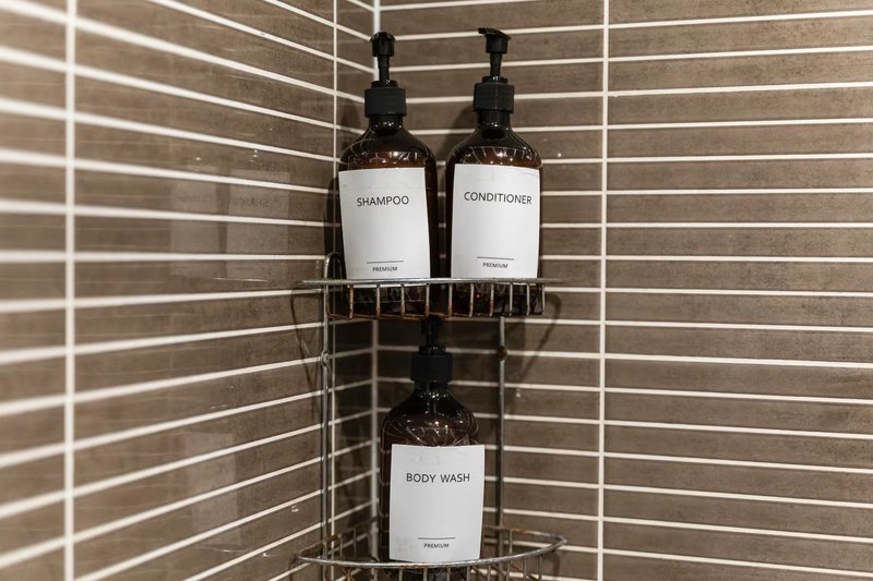 Bathroom corner shower caddy with three labeled toiletry bottles on tiled wall