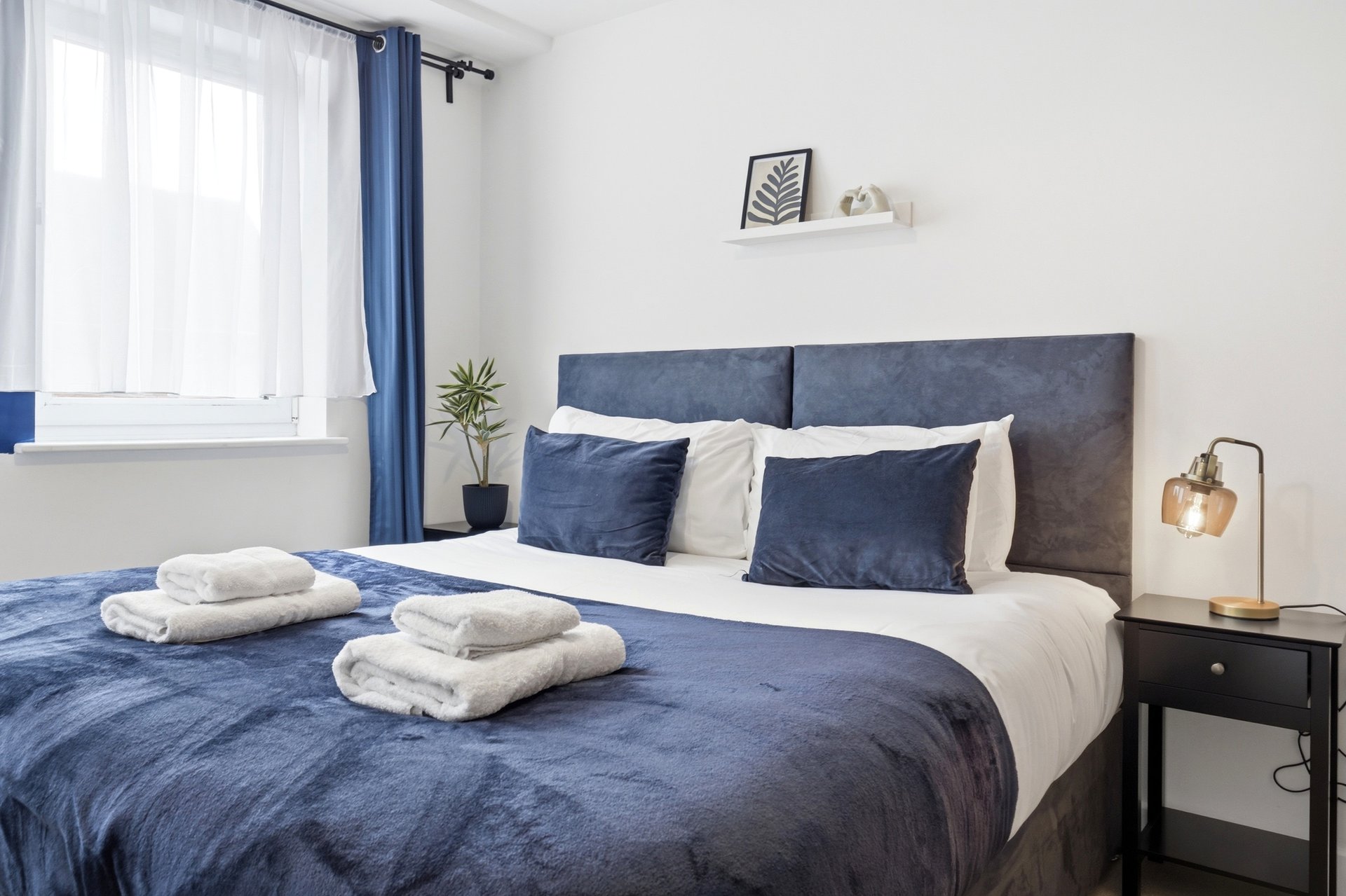 Modern bedroom with blue upholstered headboard, navy bedding, white pillows and folded towels