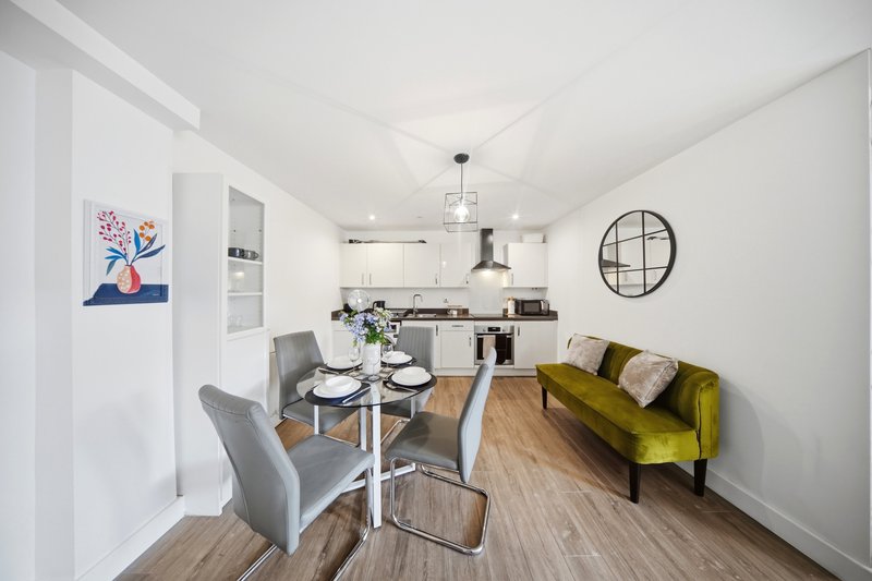 Modern open-plan kitchen and dining area with green sofa, dining table, and wall art
