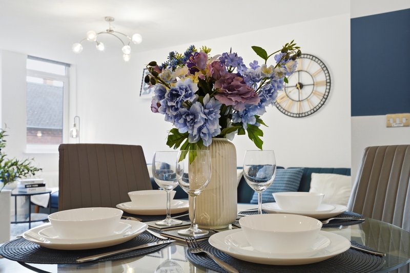 Dining table with place settings, floral centerpiece, and upholstered chairs in modern interior