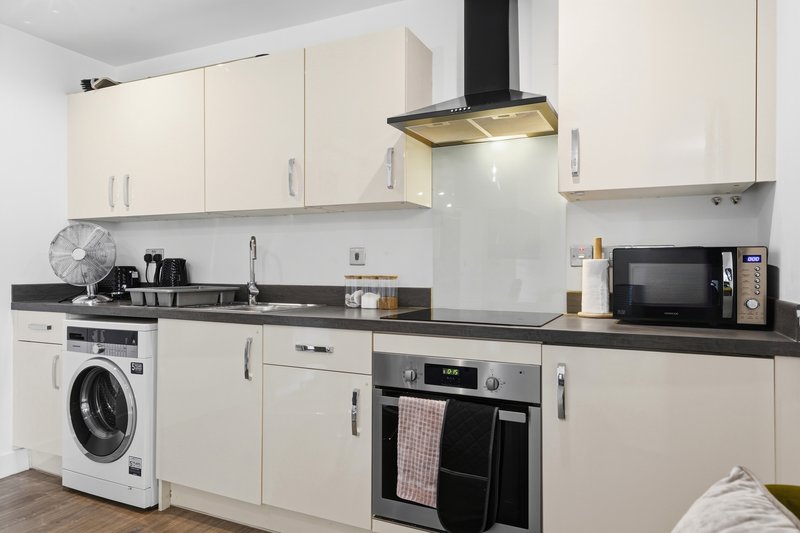 Modern kitchen with cream cabinets, black countertop, integrated appliances and range hood