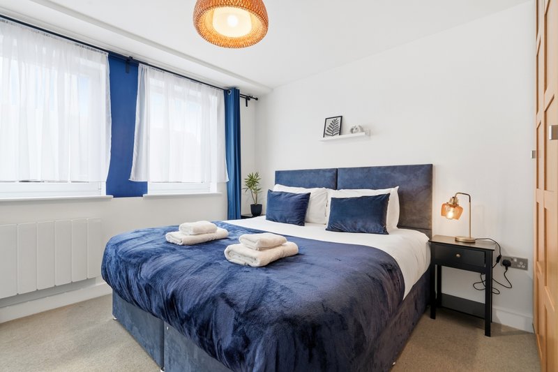 Modern bedroom with double bed, blue bedding, white pillows, pendant light and blue curtains