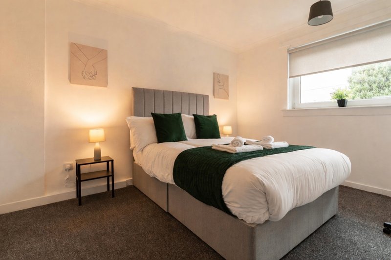 Modern bedroom with grey upholstered bed, green and cream pillows, bedside lamps and window