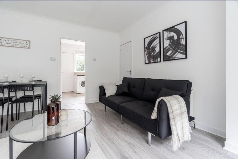 Open-plan living room with black sofa, round marble coffee table, and dining area visible through doorway