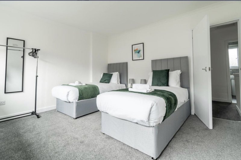 Modern twin bedroom with grey upholstered beds, white bedding, green throws and shared ensuite
