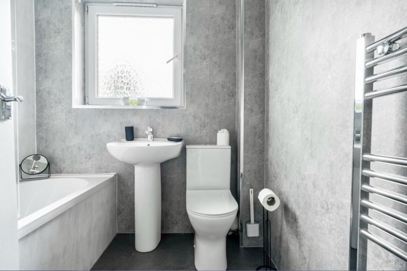Modern bathroom with pedestal sink, toilet, bathtub, heated towel rail and window