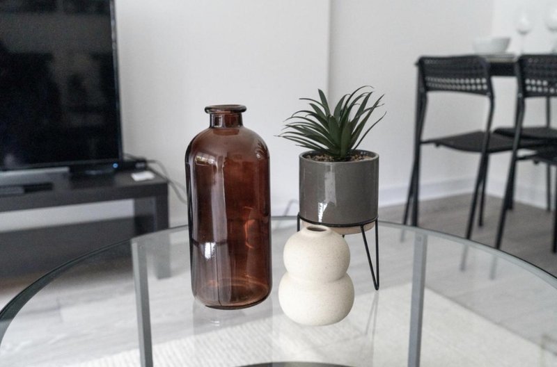 Modern living room with glass table, decorative brown bottle, potted plant, and black chairs