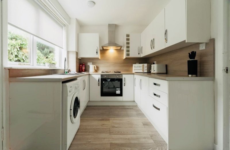 Modern kitchen with white cabinets, wooden worktops, integrated appliances and window