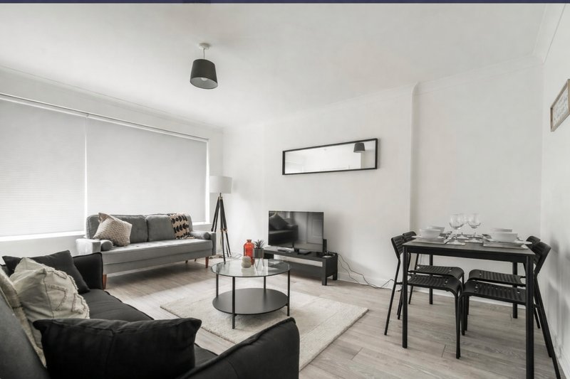 Modern living room with gray sofa, black armchair, dining table, and wall-mounted TV