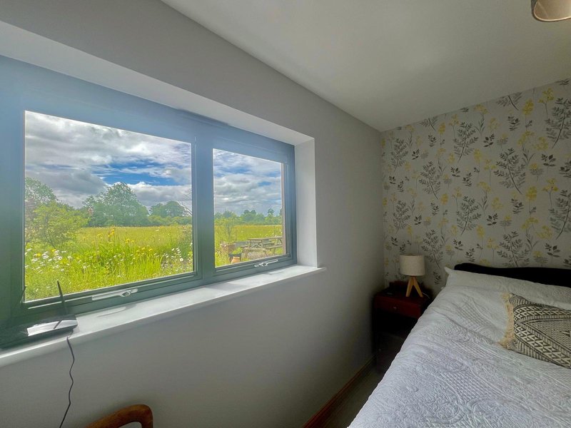 Bedroom with double bed, large window overlooking green field, floral wallpaper
