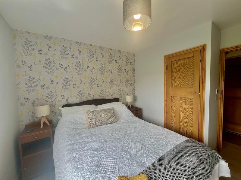 Bedroom with double bed, floral wallpaper, wooden doors, and bedside lamp