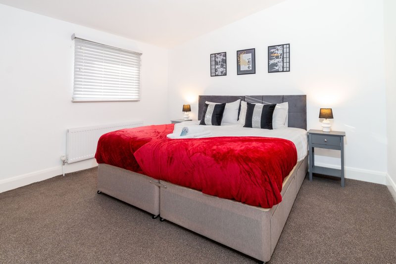 Bedroom with double bed, red duvet, striped pillows, bedside tables, and window